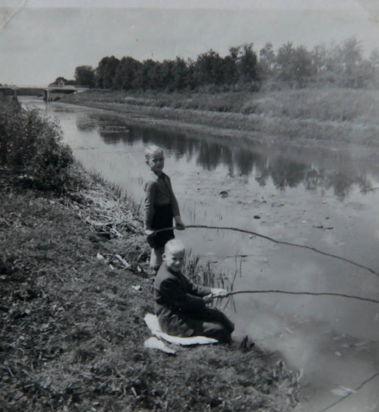 Hennie’s broers Frans en Bennie vissen met zelfgemaakte hengels in het kanaal Almelo-Nordhorn langs de Schotbroekweg. Hier, langs dit kanaal, is de wielrenner Hennie Kuiper geboren